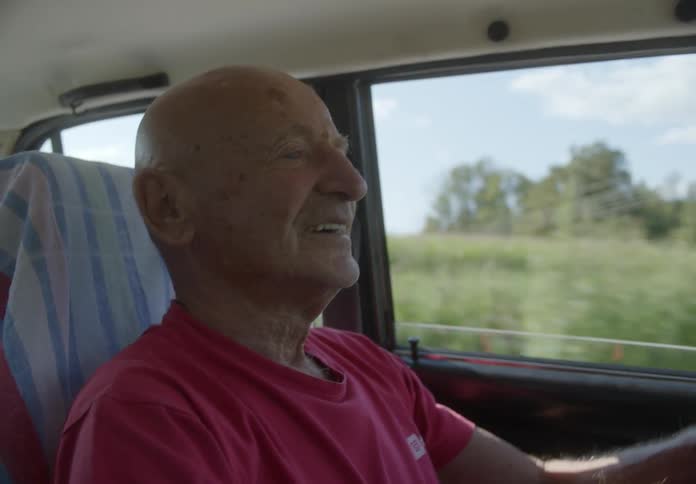 An old man driving a car and smiling