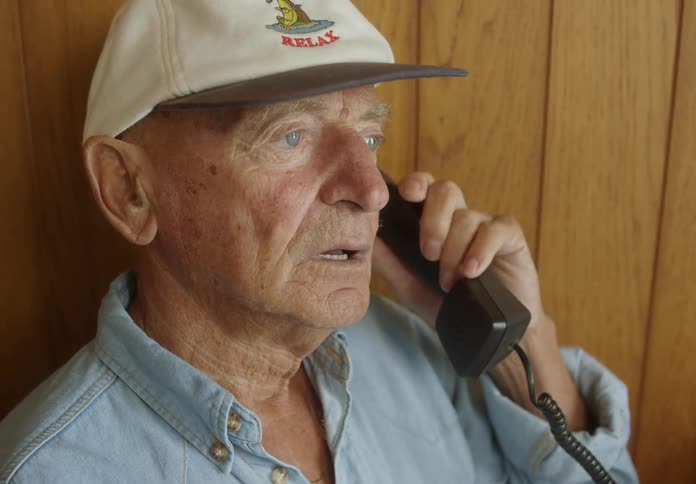 Close up of an older man sitting talking on a telephone smiling and laughing indoors on a bright day
