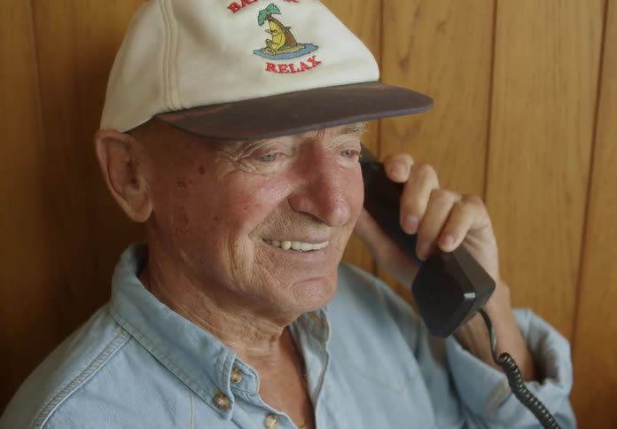 An elderly man talks on an old corded phone indoors