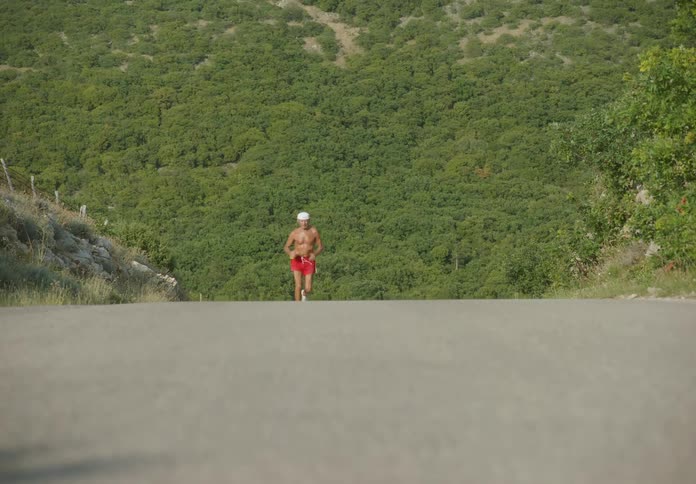 An old man running on a road with a mountain in the background