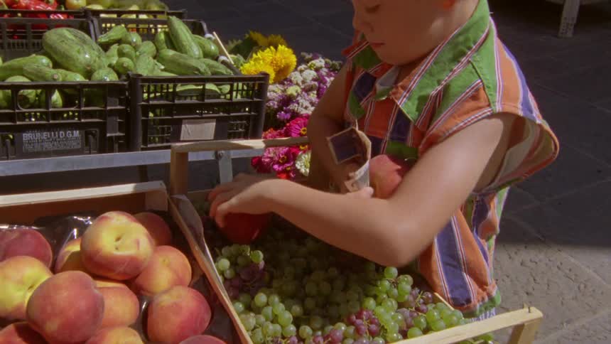 A boy picking two peaches at a grocery store and handing them over along with a money note