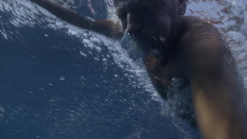 Close up from underwater of an older man swimming in the ocean on a bright day