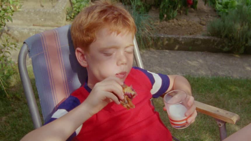 Child sitting eating food and holding a glass of milk in an outdoor environment