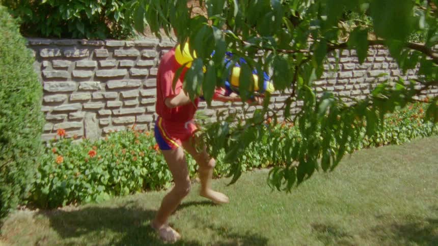 Child with red hair shirt and shorts plays with water gun in the garden