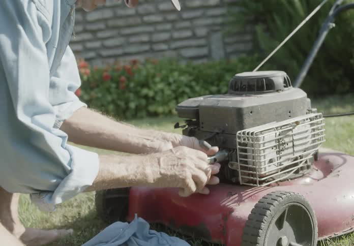 An elderly man is repairing a lawn mower in the garden