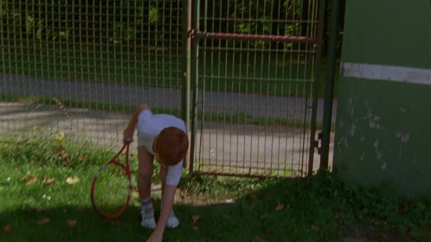 A boy enters a tennis court with a racket and a ball in his hand
