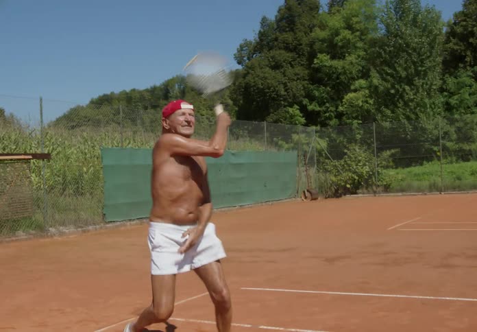 Shirtless man with a red cap playing tennis on the clay tennis court in daytime