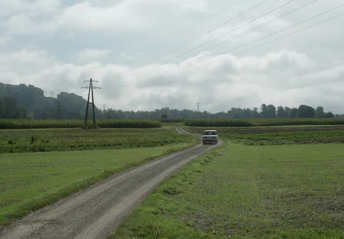 A car drives down a road between two areas of flat grassland