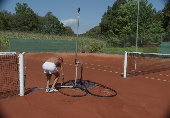 An elderly man exercises on a tennis court on a hot day