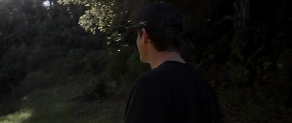 A man in black walks near some trees