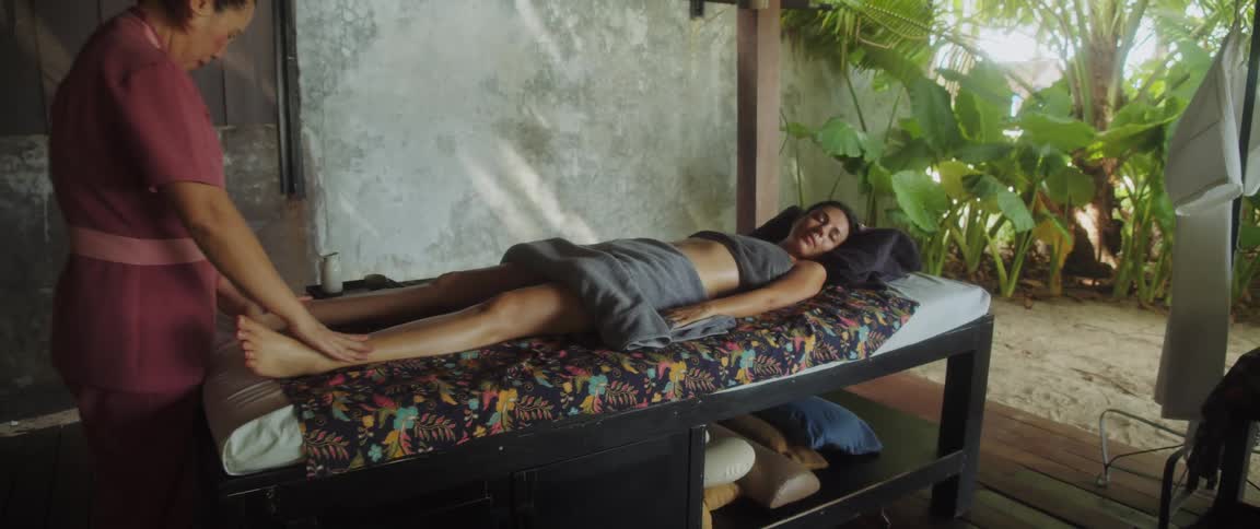 Lady laid on the bed while being massaged by an old woman