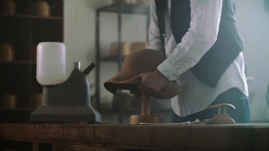 A black man wearing a jacket ring and necklace in his workshop making a hat