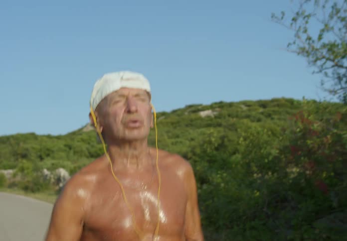 An elderly man running and sweating while listening to something on a wired headset