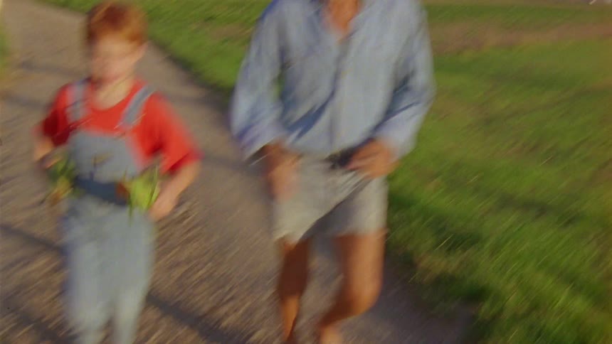 Father and son running on a walking path surrounded by grass at mid day