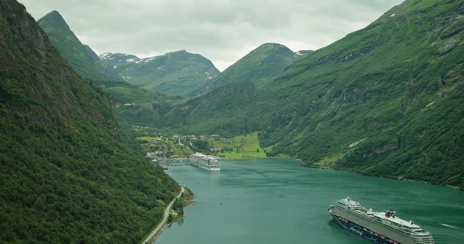 An aerial view of a lake in the middle of forested mountains where cruise ships are passing by