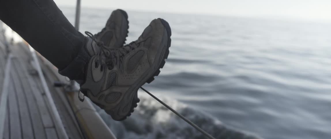 A person's feet are on the railing of a moving ship