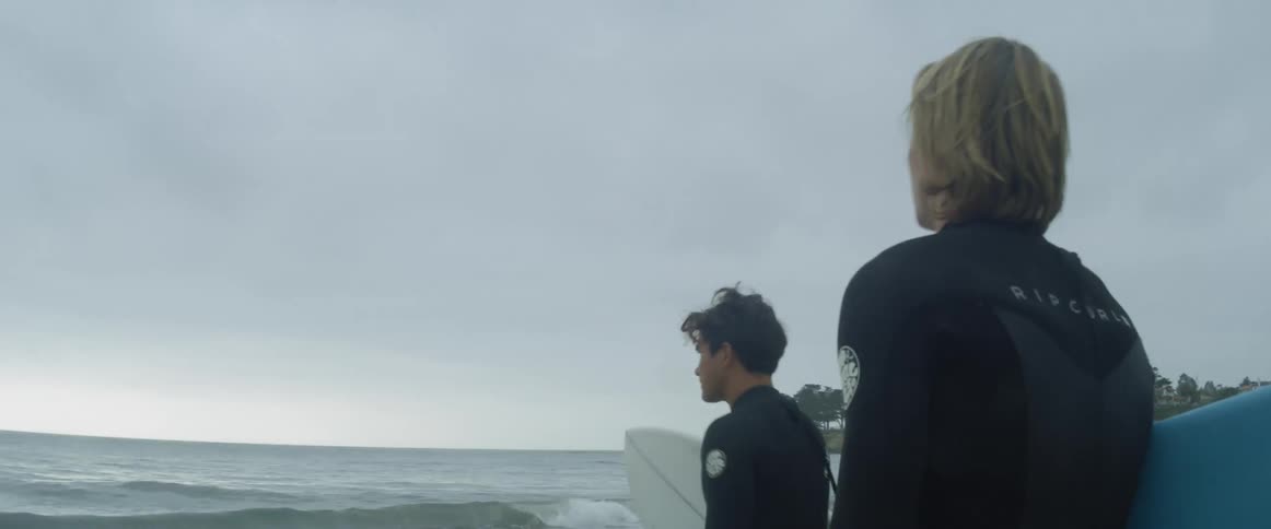 Two boys heading into the sea with their surfing board while wearing swimsuit