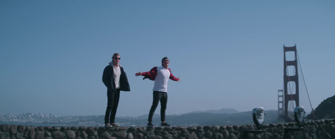 Two young men standing on a lookout point in the wind trying not to fall