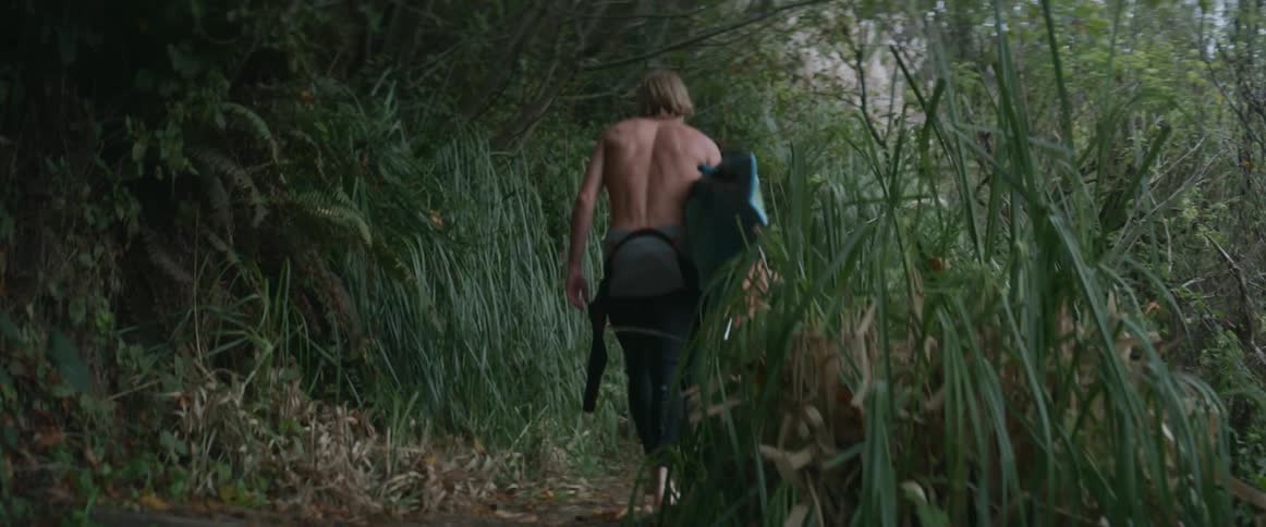 Two muscular young men carry surfboards through the wilderness