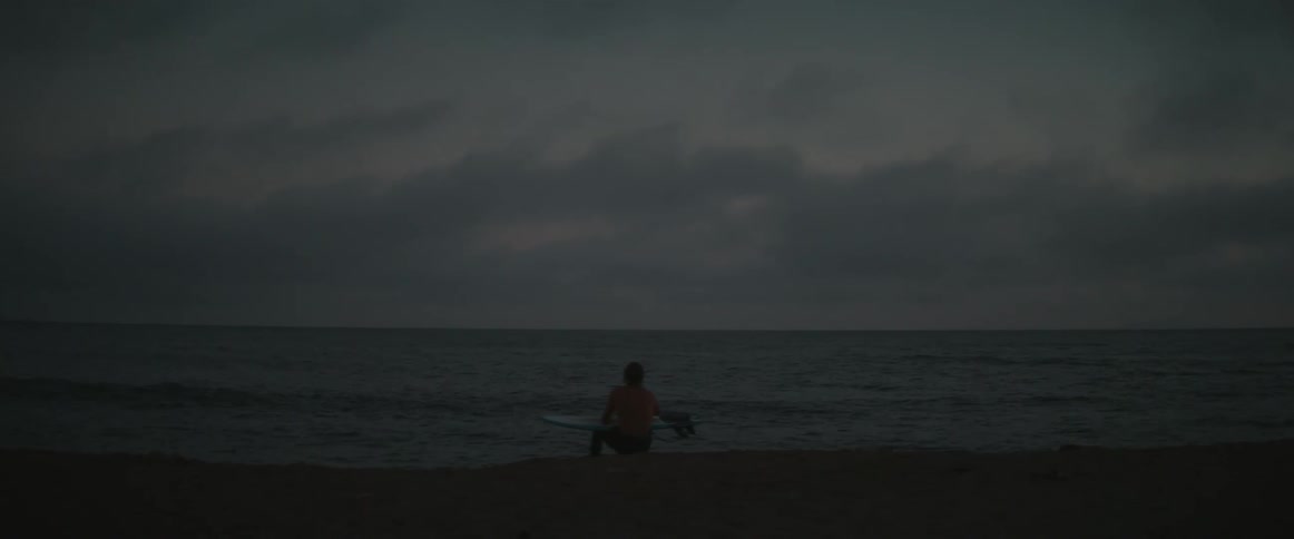 A surfer sits by the sea holding his board