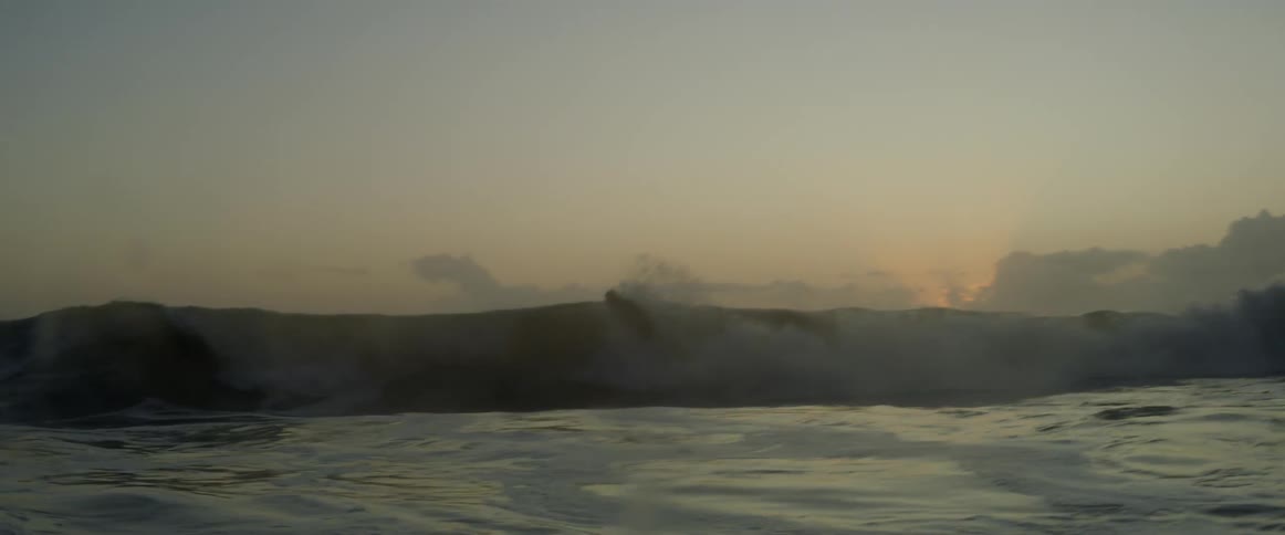 A man dropping in and surfing a wave with the sunrise on the horizon