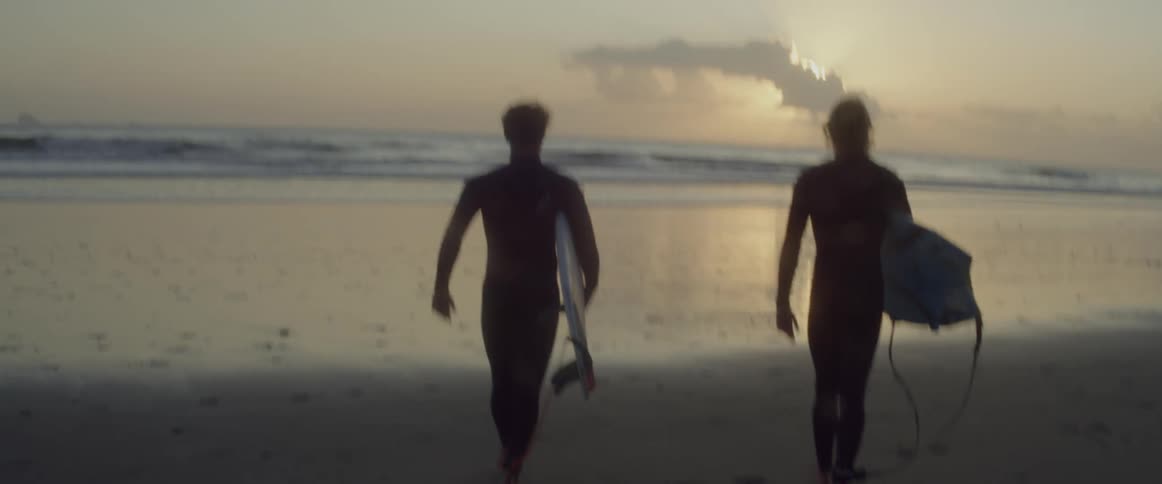 Two surfers talk to each other as the walk into the sea with their boards