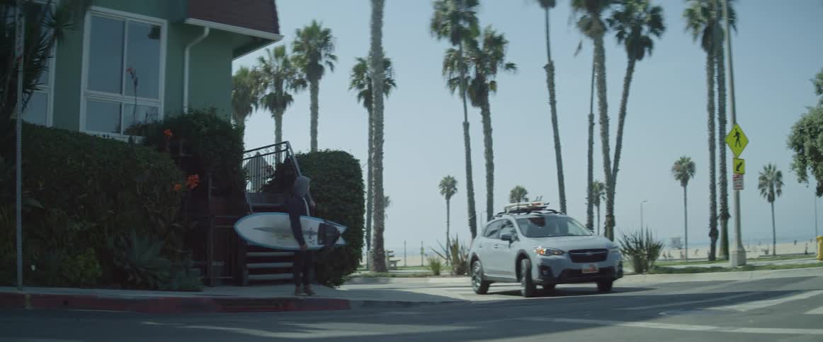 A male surfer waits at a street corner near the beach for his ride to arrive and pull over