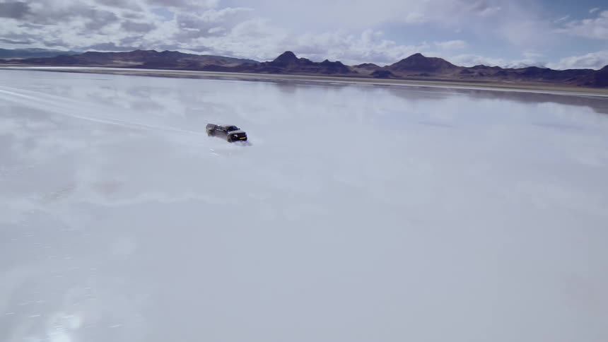 A truck off road driving through flooded salt flats, a landscape on a cloudy day, fpv footage