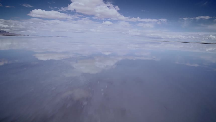 Aerial of the calm surface of the flooded salt flats under a blue sky, FPV drone footage