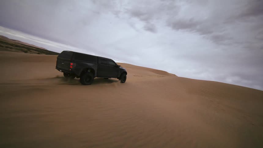 A truck driving over sand dunes in the desert, fpv drone footage