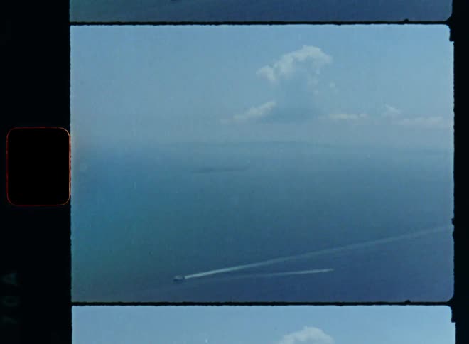 Aerial vintage film footage of a ship or boat sailing in the open sea transporting freight or cargo from overseas symbolizing globalization on a sunny day with bright sky and blue water