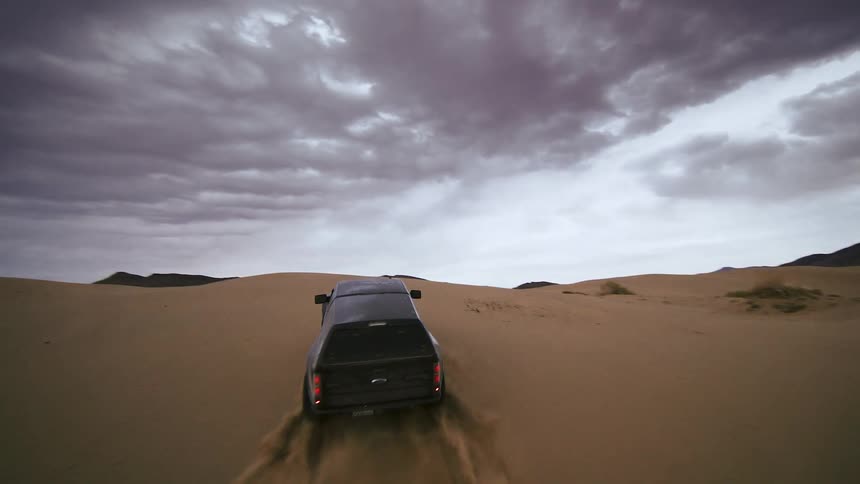 FPV drone footage of a black truck climbing sand dunes on the desert