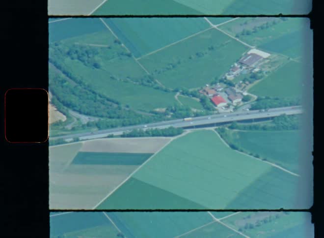 Aerial view of a road or highway as cars drive on the street in a rural area with forests and agricultural farm fields next to some large industrial buildings with infrastructure surrounding them