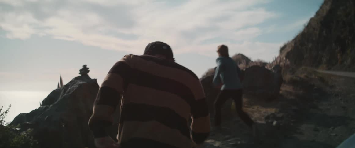 A car parked outdoors as two men get out of it and walk over to a rock edge over looking the coast