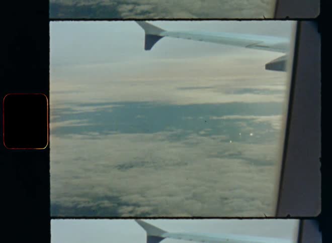 Retro POV film footage looking out of the window of an airplane on the wing while flying over rural landscape partially covered by clouds with forest fields and towns as the sun shines above the cloud cover