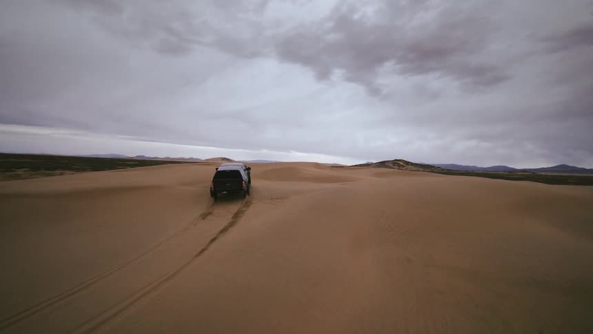 FPV drone view of a truck driving over sand dunes in the middle of the day in the desert
