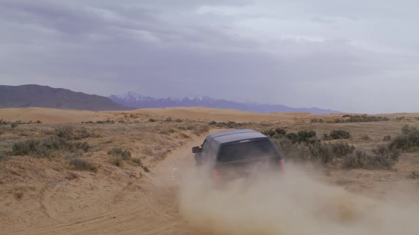 A truck takes a sharp turn around a bend in a dirt road through the desert at high speed