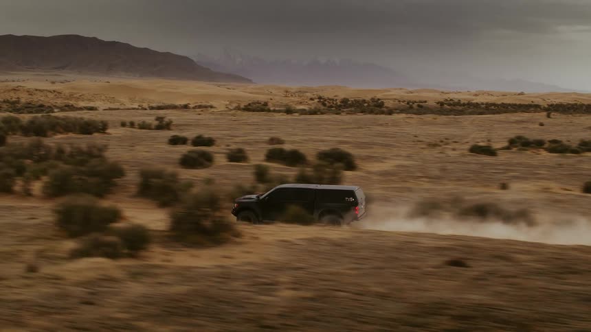 A truck races through the desert, kicking up dust, high-speed aerial footage