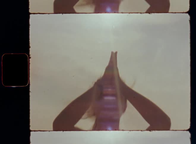 The hand of young brown-haired woman moves in dynamic motion through the warm air on a windy day with a mild breeze during a meditation or zen yoga session outside by the shore of a lake or ocean and the sun shines onto the rippling surface of the water