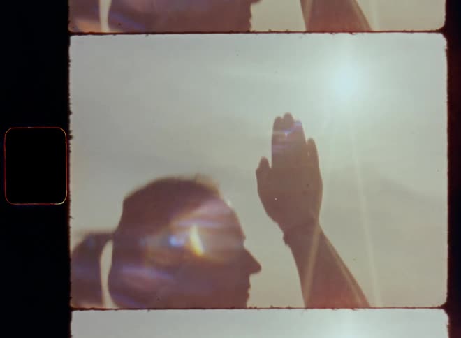 Hand held retro film footage of woman doing yoga or meditating outside in nature as she raises her arms and joins her hands together in front of her face with closed eyes to find zen and inspiration with high spirits and spiritual rituals on a windy day