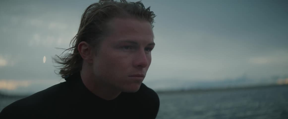 A young surfer nods and blinks as he looks at the sea