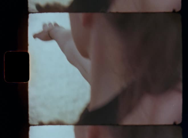 Dynamic Super 8 close up of a brunette womans muscular arms outstretched wearing a black sports top while doing yoga or Pilates as she looks into the setting sun shining at the horizon on the ocean on a gloomy overcast summer day