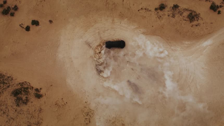 An offroad truck doing donuts in the middle of the desert creating dust clouds blowing away, aerial footage