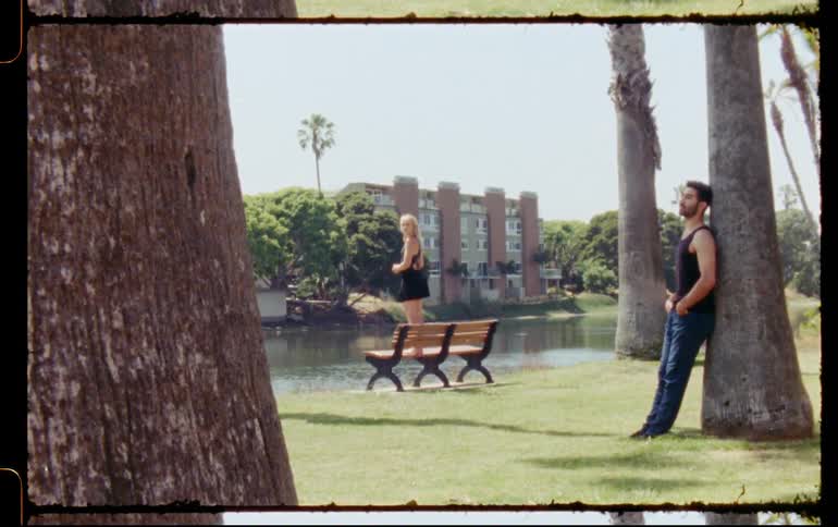A man leaning against a tree and a woman standing on a bench