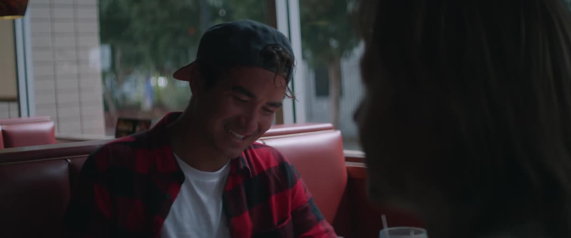 A man sitting in a restaurant booth talking and laughing with someone across from him while they eat