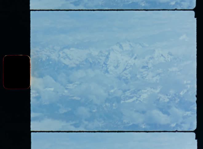 Aerial drone footage on Super 8 film of the steep hills and mountains with snow and ice on top and glaciers in the valleys between the high peaks and summits during the day