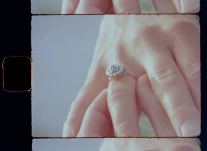 A silver and posh diamond engagement ring that is adorned with many gemstones is placed on the finger of a hand of a woman wearing a green dress in the sunshine after a romantic proposal as celebration of love and a happy relationship