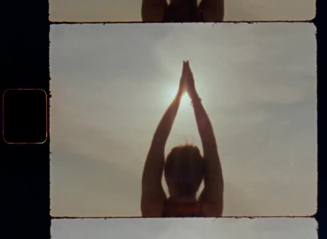Woman with black leggings and shirt raises her arms in yoga movements towards the sun in the sky and the bright sunlight flares and shines onto her sportive body connected to her mind through sports such as Pilates or meditation