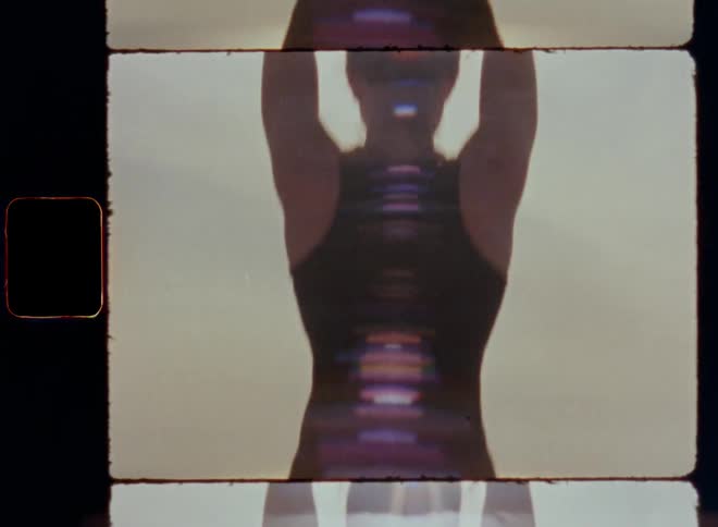 Tilting Super 8mm shot of a sportive woman doing tree or mountain yoga pose standing on one foot on concrete building next to the ocean as the sun shines brightly and the wind or breeze moves her swaying hair while she trains body balance and strength