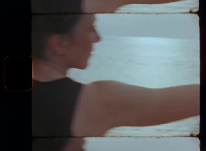Attractive woman in black top doing yoga facing the sea with her arms open and raised parallel to the horizon in the warrior pose representing strength power persistence and endurance with dynamic camera movement on old Super 8mm film material